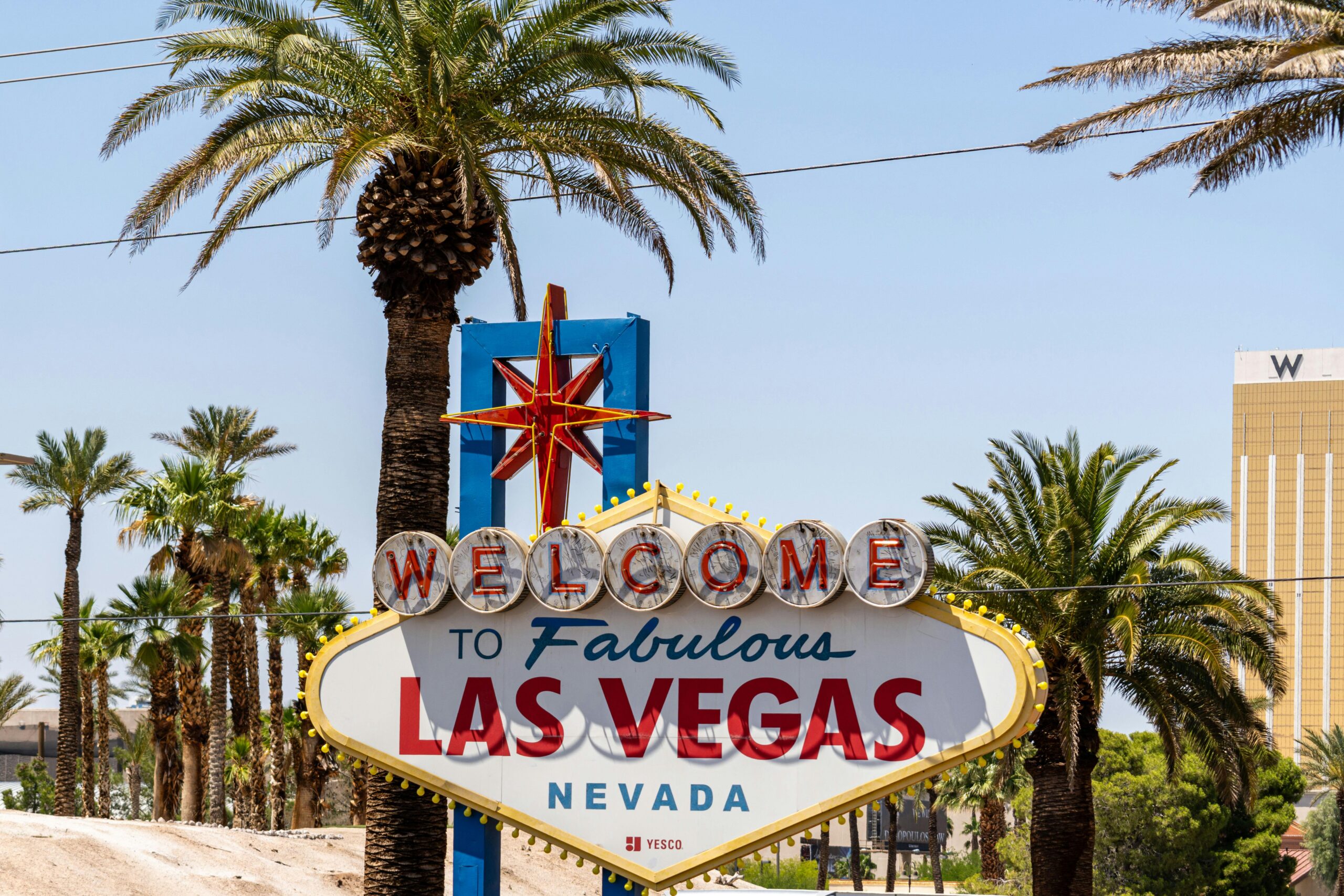 The classic 'Welcome to Las Vegas' sign amidst palm trees, under a bright blue sky.